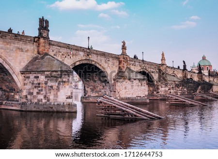 Photo of the famous Prague landmark Gothic Charles bridge taken during the spring from the side of the river Vltava with a blue sky in the background 