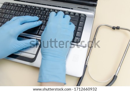 hands of a female doctor in blue medical gloves are working at a laptop close-up, next to a stethoscope.
