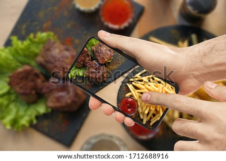 Food blogger taking picture of delicious shish kebab and french fries at table, closeup