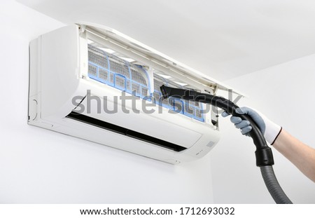 A worker is using a vacuum cleaner to clean the air conditioner.Air conditioner system on white wall room. Air conditioning.A white air conditioner is installed on a white wall in the apartment.
 Royalty-Free Stock Photo #1712693032