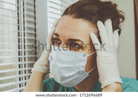 A medical professional in a surgical protective mask looks exhausted after a busy shift in the hospital during a coronavirus epidemic.