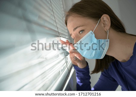 young female wearing face mask and looking out of window

