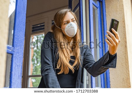 Coronavirus concept. Sick pretty woman with mask talking on phone in the window at home in morning sunlight. Isolated at home video call with family and friends. Quarantine prevention to infection.