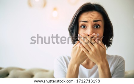 Delicate problem. Close-up photo of a worried woman, who is covering her mouth with her hands while looking in the camera. Royalty-Free Stock Photo #1712713198