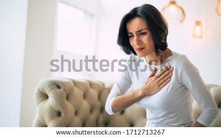 Pressure in the chest. Close-up photo of a stressed woman who is suffering from a chest pain and touching her heart area. Royalty-Free Stock Photo #1712713267