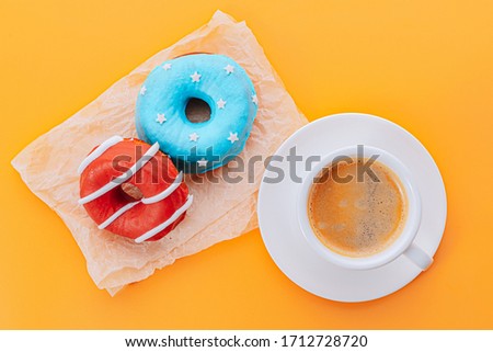 donuts one with blue icing and white stars and with red icing and white stripes and a cup of coffee on a yellow background