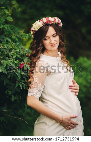 Portrait of a pregnant woman on green nature background. Young beautiful pregnant girl with a wreath of flowers on her head. Motherhood. Spring. copy space. selective focus.