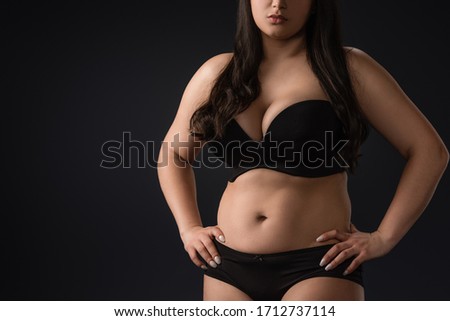 Cropped view of young size plus woman in underwear on black background