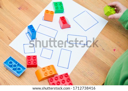 Match to correct shape. Boy placing toy blocks on white paper with defined lines. Toddler education. Early exercise, for preschool children.