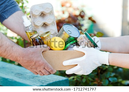 Donation box with various food. A volunteer passes a cardboard box with dry cereals, canned goods, eggs, oil. From hand to hand. Help during a pandemic. Food donations or food delivery concept. Royalty-Free Stock Photo #1712741797