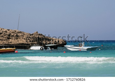 Seascape with boat by stone coast of Cyprus island and blue turbulent sea on sunny windy summer day
