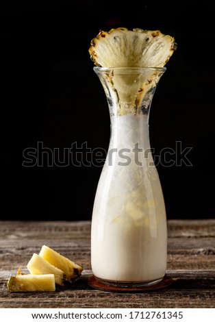 Pina Colada in a vase like glassware with artistic presentation of pineapple on wooden table. Photography best use for magazine or book menu concept.