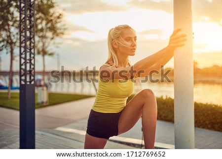 Young sporty woman stretching on a sidewalk near the river in sunrise / sunset time.