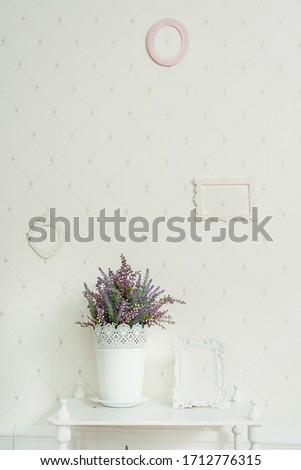 Lavender in a white pot on the shelf. Beautifully artificial lavender in a vase on a white bookcase in a room in the style of shabby chic. Empty frames on the wall details Interior in a classic style