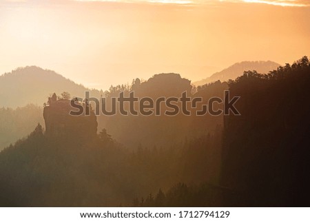 Rocky blocks and walls above valley full of thick mist. Red and orange sunrays colored mist.