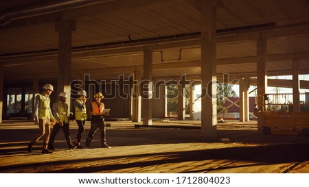 Diverse Team of Specialists Walk Through Garage Level of Industrial / Commercial Building Construction Site. Real Estate Project with Civil Engineer, Investor and Worker. Skyscraper Formwork Frames Royalty-Free Stock Photo #1712804023