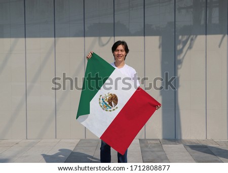 The man is holding Mexico flag in his hands on grey background.