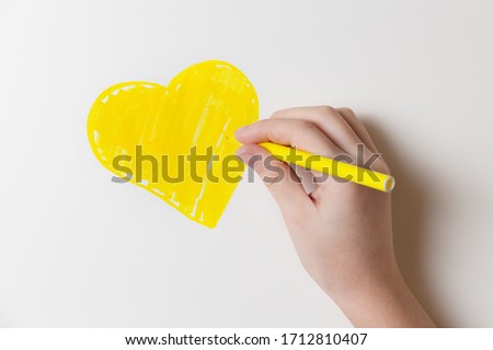 Girl draws a felt-tip pen a yellow heart on the wall of the room. Health and happy childhood concept.