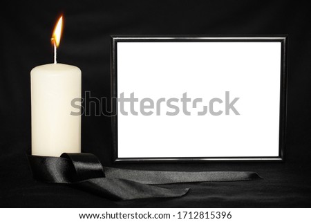 A burning white candle, a mourning ribbon, and a black frame with space for text on a black background