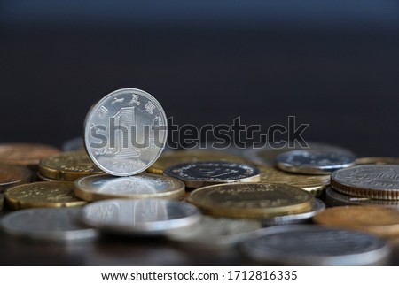 One silver-colored Chinese Yuan coin stands above coins of other countries lying on wooden table. Theme of exchange rate changes.