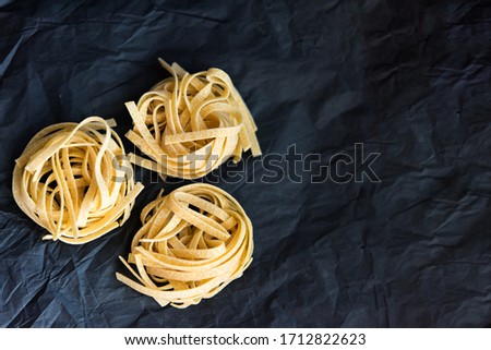 Picture of three pieces of traditional Italian raw uncooked pasta Tagliatelle on black crumpled paper background, selective focus. Vegetarian food. Nutrition concept. Italian kitchen. Preparation