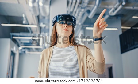 Young Hipster Woman in Holographic Augmented Reality Glasses Standing in Empty Office and Map it. Sunlight Shines Through Big Windows. Royalty-Free Stock Photo #1712828761