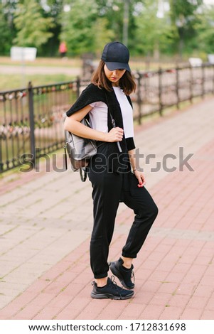 Beautiful stylish brunette girl in a white T-shirt and black pants with a backpack on his shoulder. Vertical photo