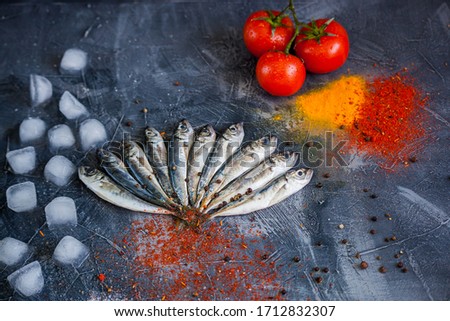 
small sea fish horse mackerel on ice with tomatoes with spices