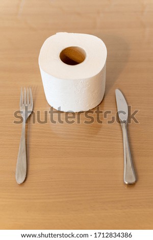 Horizontal image of toilet paper roll on brown table for background. Toilet paper without a plate. Toilet roll on brown. Knife and fork. Time of crisis, world economic collapse. 