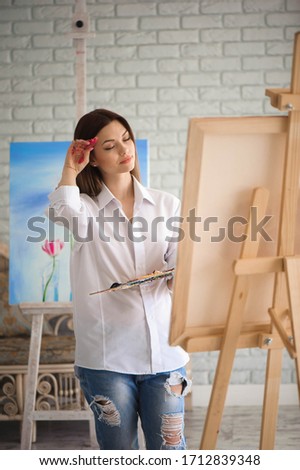 woman paints picture on canvas with oil paints in her studio