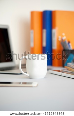 White Coffee Mug on co-working station in the office with document files and desktop monitor as blur background in vertical format.