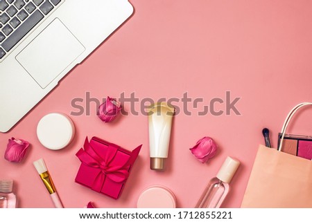 Concept of online shopping cosmetics. Top view on cosmetics bottles, cream, soap, makeup brushes, computer, paper bag on a pink background, flat lay, copy space.Layout for online cosmetics store