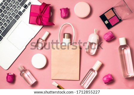 Concept of online shopping cosmetics. Top view on cosmetics bottles, cream, soap, makeup brushes, computer, paper bag on a pink background, flat lay, copy space.Layout for online cosmetics store
