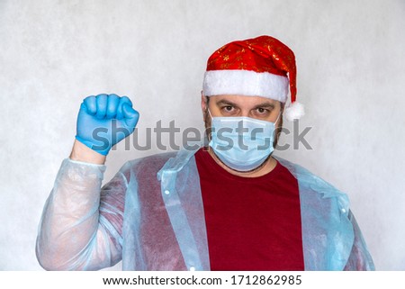 man in a Santa Claus costume and a medical mask. end of quarantine, pandemic of the coronavirus. hand with medical glove doing the Victory gesture, symbolizing the win over COVID-19.  copy space