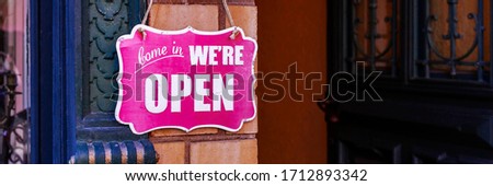 Come in We're open text on vintage pink sign at the entrance with open ancient door, banner