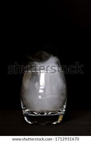 A glass full of smoke stands on a black surface with strong contrasts - smoke stops in a glass against a black background - mystical and dark picture with smoke and glass