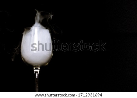 A glass full of smoke stands on a black surface with strong contrasts - smoke stops in a glass against a black background - mystical and dark picture with smoke and glass