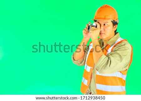 Foreman wearing safety helmet with safety vest take picture with a camera on over green screen background.