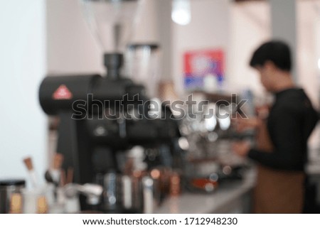 Blurred picture taking behind the bar of a male barista in uniform making coffee with the machine.