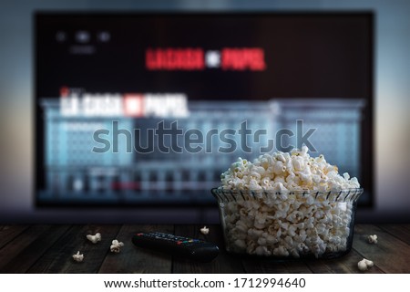Video streaming app on tv screen behind a bowl of popcorn and a remote control. Royalty-Free Stock Photo #1712994640