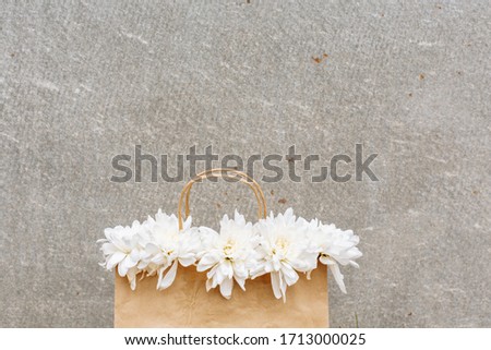 a paper bag with white chrysanthemums against a gray wall. space for text