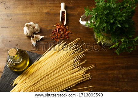Close up angle view of the typical italian recipe spaghetti aglio olio e peperoncino (garlic, oil and hot pepper) ingredients with a glass jar with sprigs of parsley on wooden table Royalty-Free Stock Photo #1713005590
