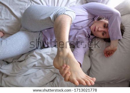 Caucasian woman looking on her hairy leg resting on bed at home. She can not do depilation in quarantine. Top view.