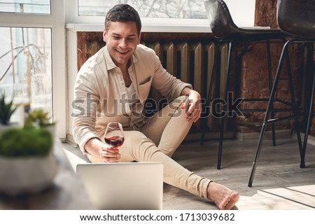 Virtual party. Pleased man lifting a glass of red wine in front of his laptop Royalty-Free Stock Photo #1713039682