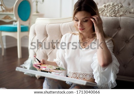 Beautiful woman artist drawing her picture on canvas with oil colors at home