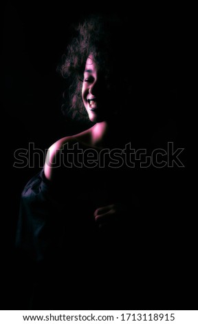 A creatively processed photo of a beautiful Afro-American girl with curly hair who poses in the studio on a dark background.
