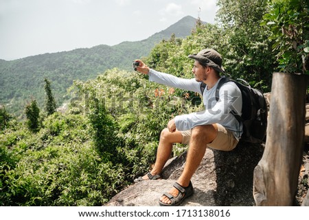 male traveler is filming a panorama of the landscape of forests and mountains on a video camera. Sports activities and video.