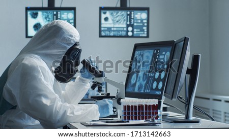 Scientist in protection suit and masks working in research lab using laboratory equipment: microscopes, test tubes. Coronavirus 2019-ncov hazard, pharmaceutical discovery, bacteriology and virology. Royalty-Free Stock Photo #1713142663