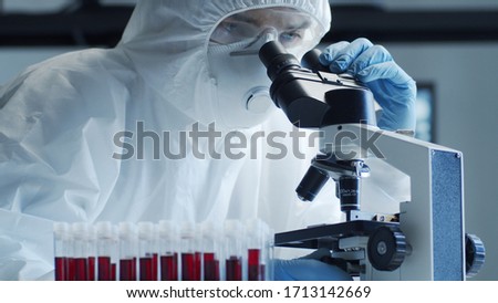 Scientist in protection suit and masks working in research lab using laboratory equipment: microscopes, test tubes. Coronavirus 2019-ncov hazard, pharmaceutical discovery, bacteriology and virology. Royalty-Free Stock Photo #1713142669