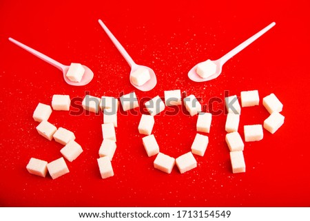 out of sugar cubes written word stop,plastic spoons in a piece of refined sugar on a red background.Tell stop sweet Royalty-Free Stock Photo #1713154549